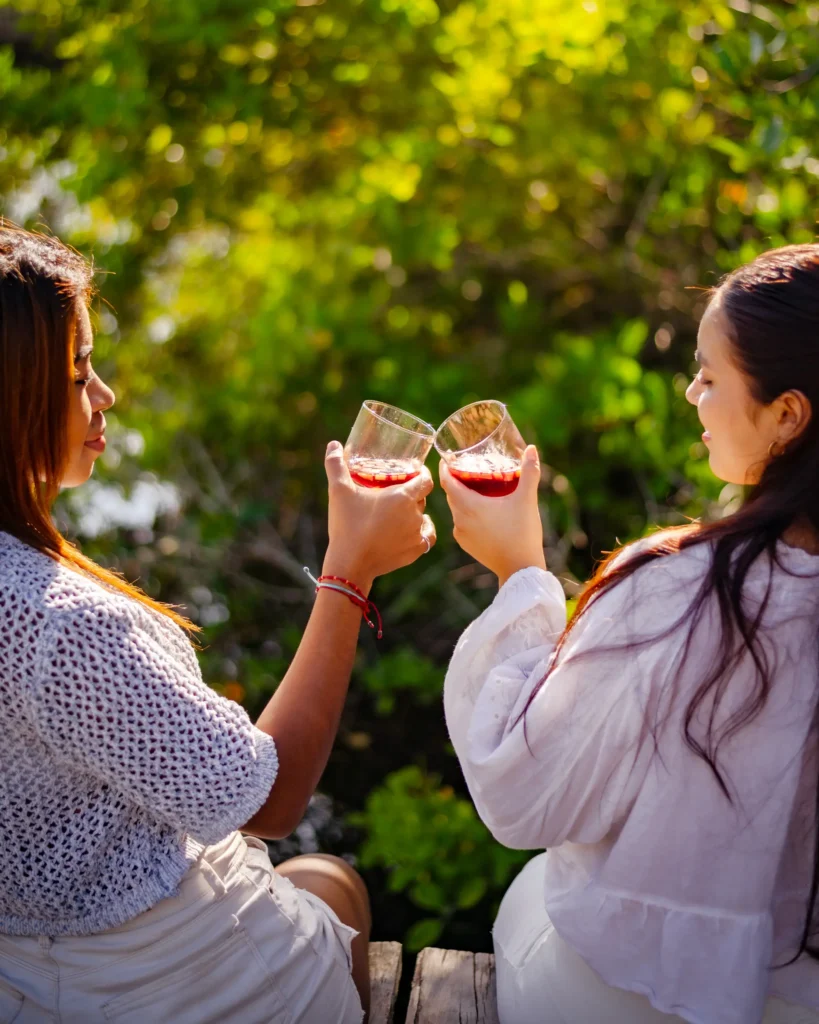 Dos mujeres sentadas al aire libre hacen un brindis con copas de sangría Sangridom, rodeadas de vegetación.